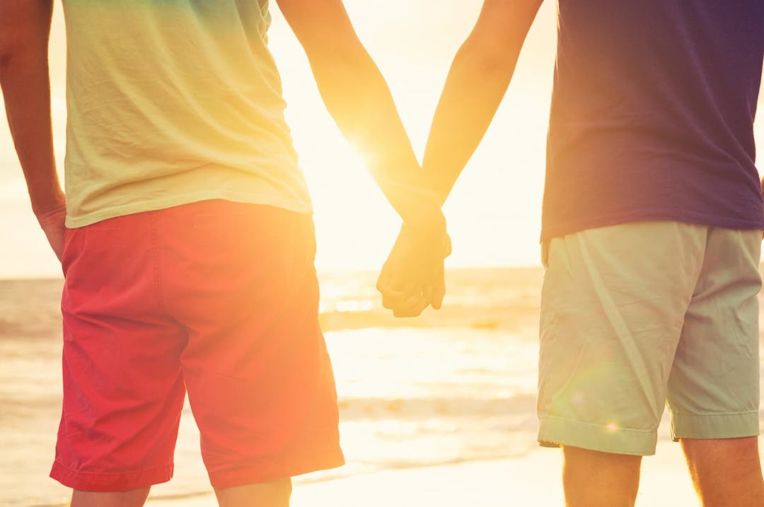 Gay couple holding hands by the beach